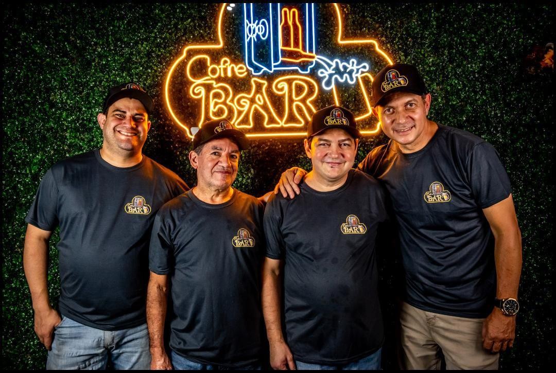 Os quatro sócios do Cofre Bar em frente ao letreiro de neon do bar